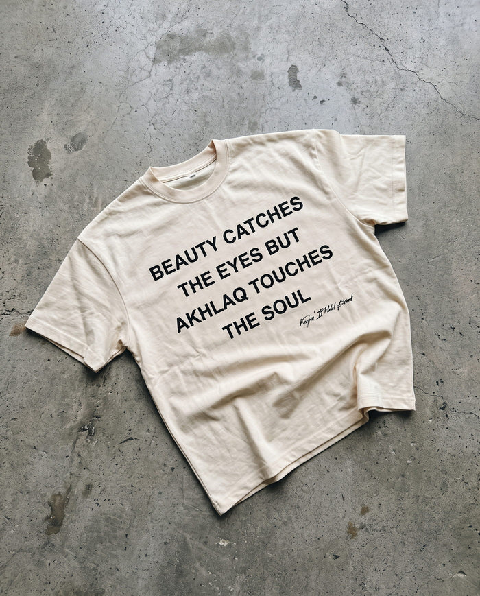 Akhlaq Over Beauty natural boxy tee laid flat on concrete