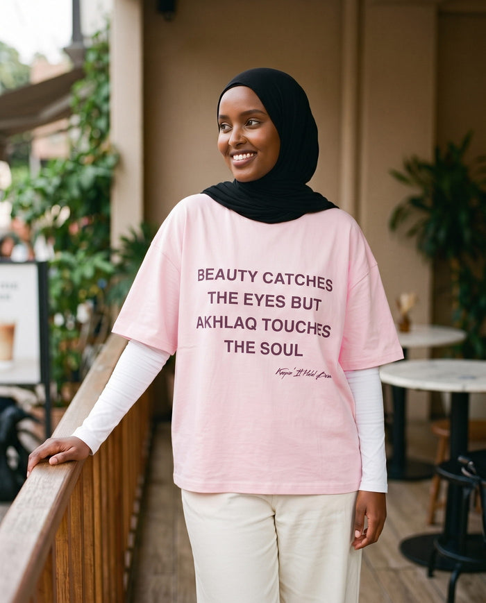 Akhlaq Over Beauty soft pink boxy tee on a cafe balcony