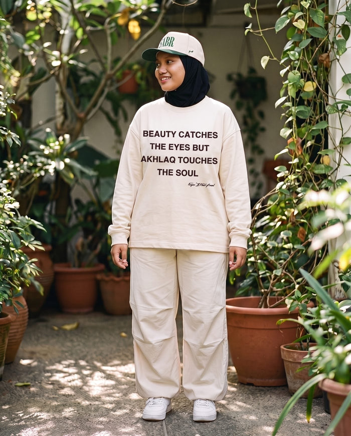 Akhlaq Over Beauty bone long sleeve on a plant-filled patio