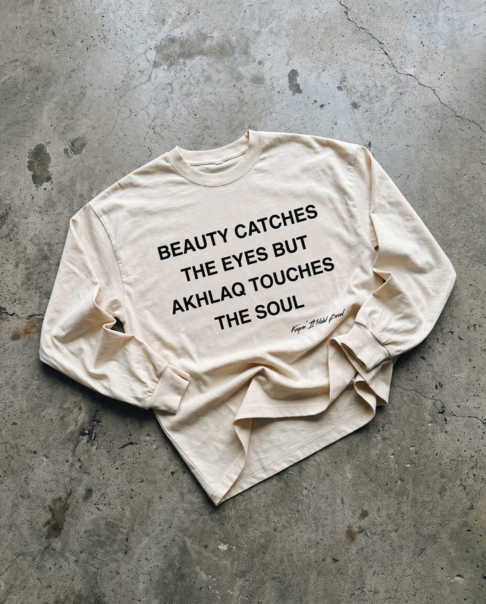 Akhlaq Over Beauty bone long sleeve laid flat on concrete