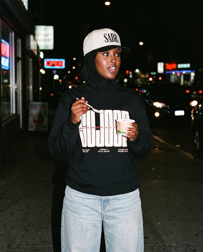 Sujood for the Heart black long sleeve on a neon-lit night street