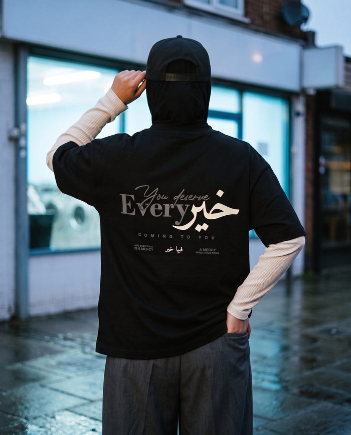 You Deserve Every Khayr black boxy tee back print outside a launderette at dusk
