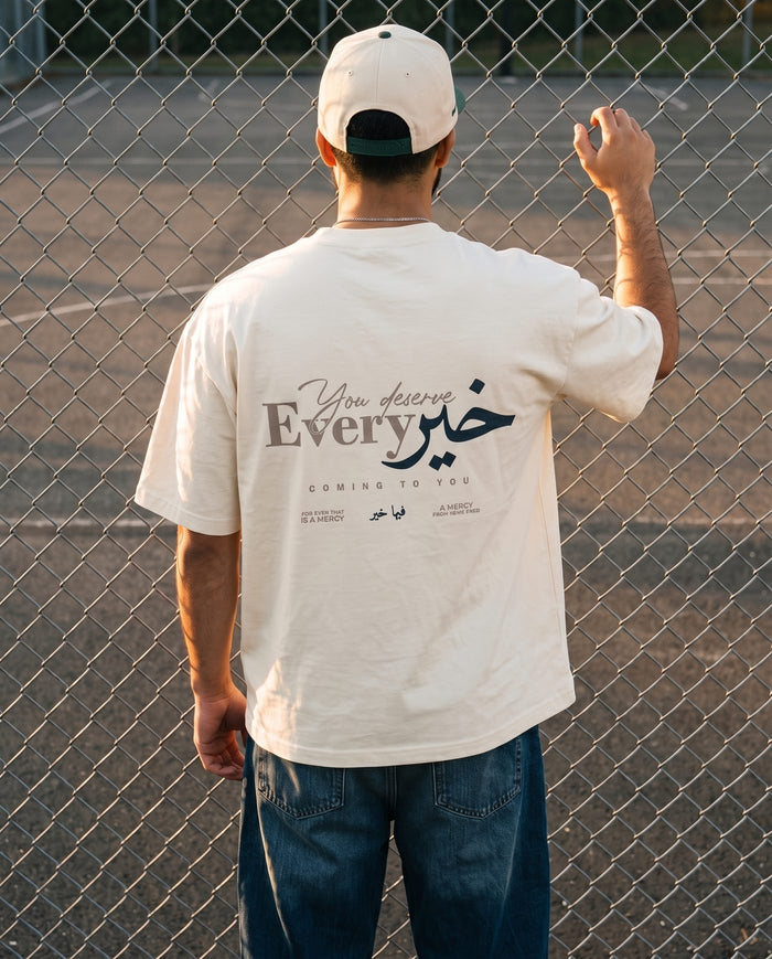 You Deserve Every Khayr natural boxy tee back print at a court fence in golden hour