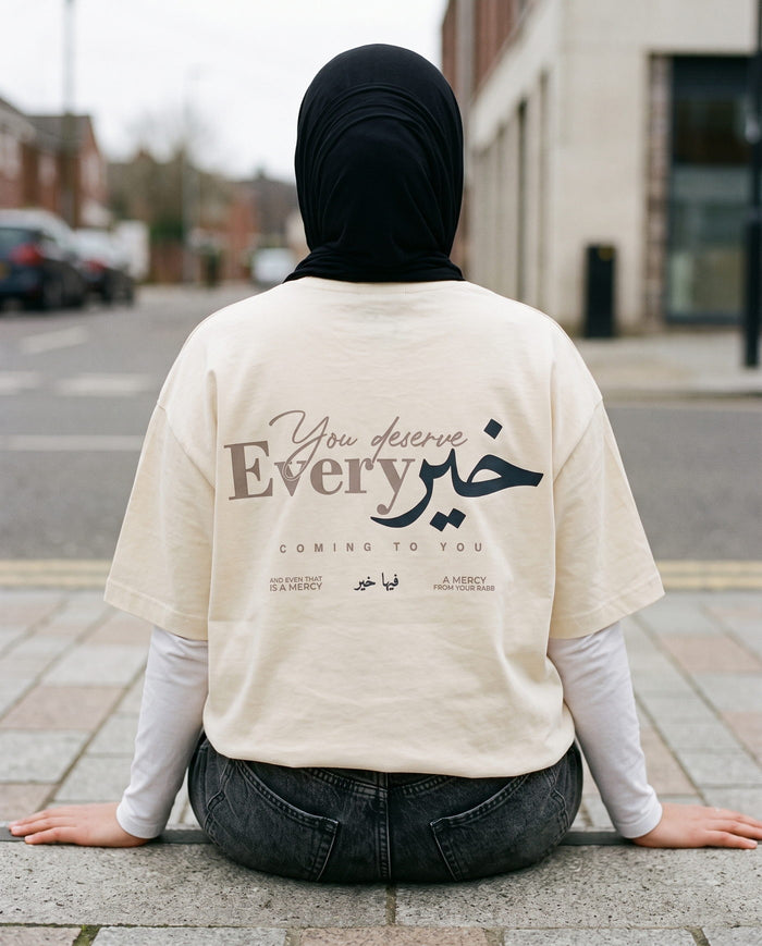You Deserve Every Khayr natural boxy tee back print, seated on a kerb