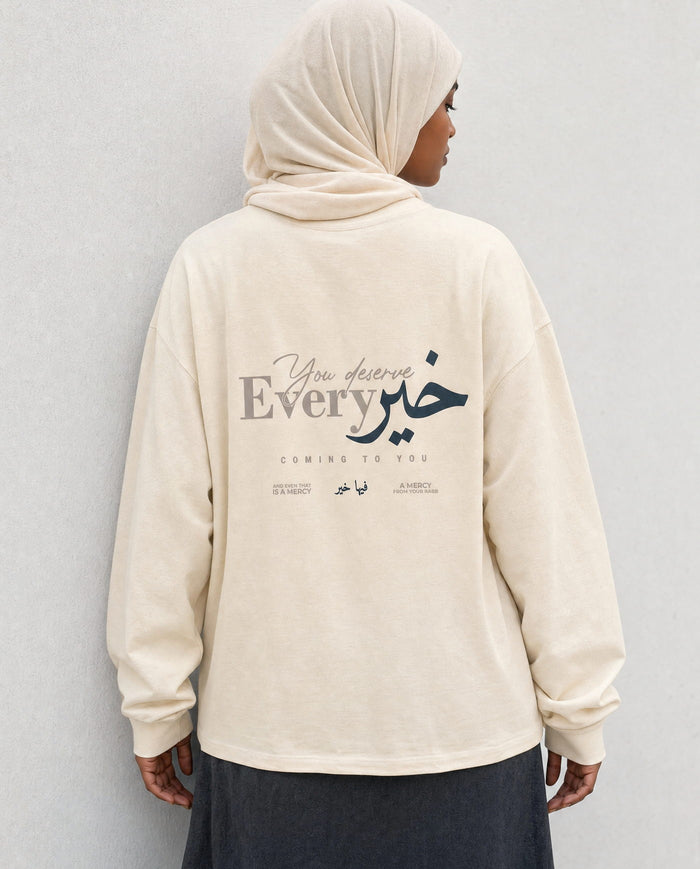 You Deserve Every Khayr bone long sleeve back print, leaning on a wall