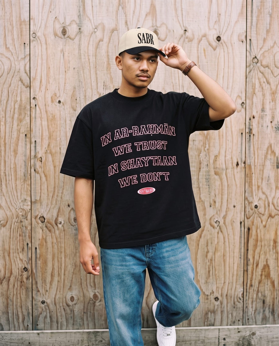In Ar-Rahman We Trust black boxy tee against plywood hoarding