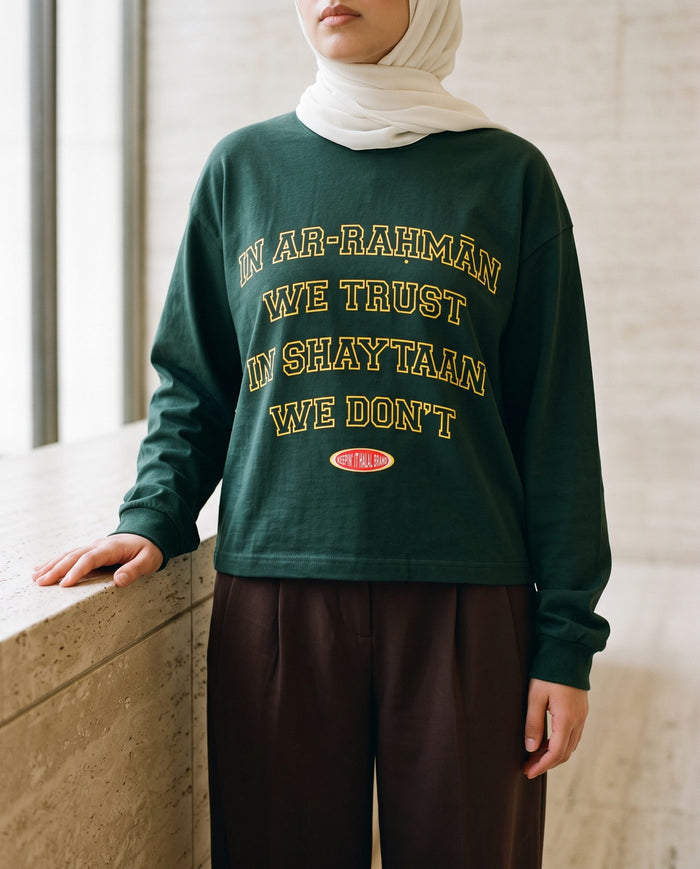 In Ar-Rahman We Trust hunter green long sleeve in a travertine lobby