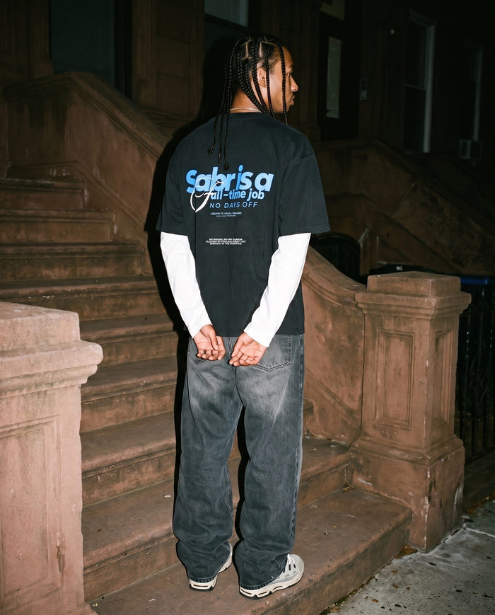 Full-Time Sabr black boxy tee, back print, hands clasped on a stoop at night
