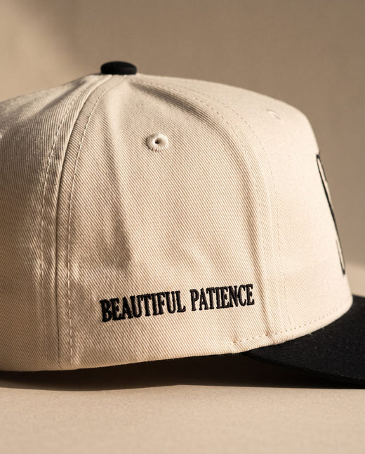 Close detail of BEAUTIFUL PATIENCE embroidered in black on the right side panel of the ivory Sabr Cap