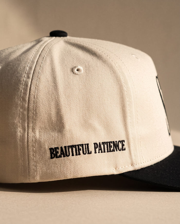 Close detail of BEAUTIFUL PATIENCE embroidered in black on the right side panel of the ivory Sabr Cap