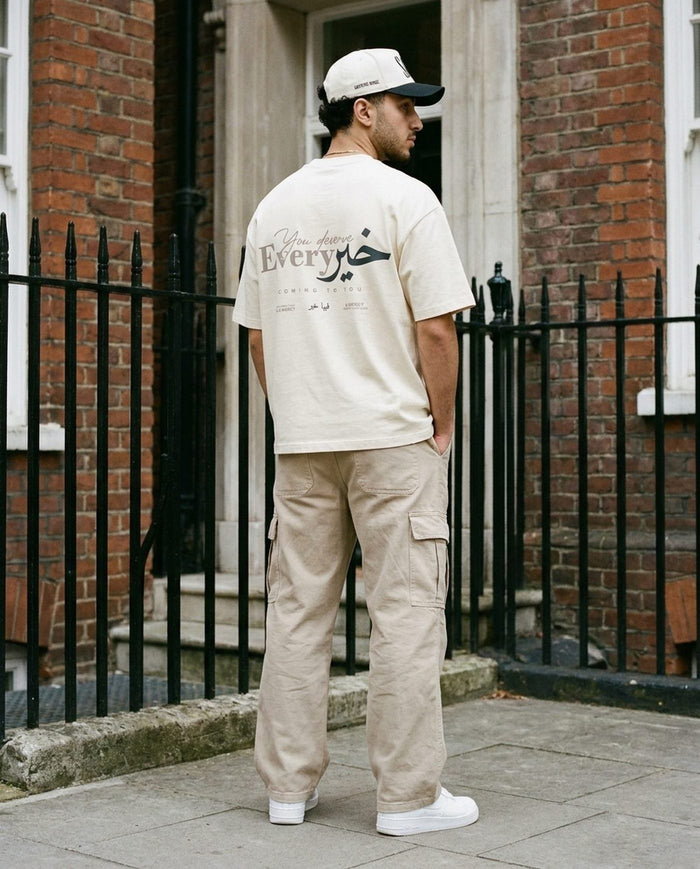 Sabr Cap in ivory with a black brim worn with the natural You Deserve Every Khayr tee on a railed London street