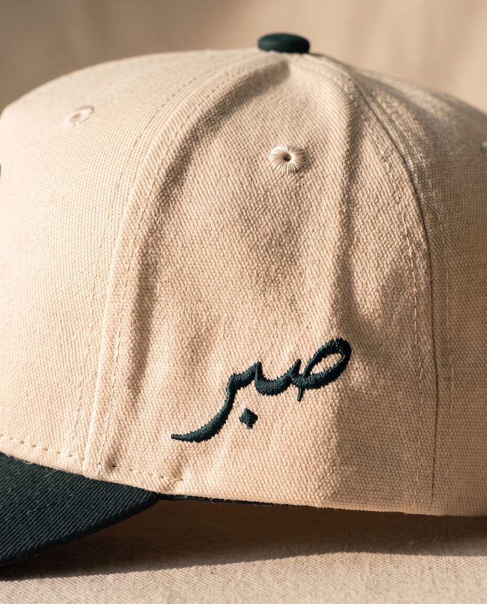 Close detail of the Arabic word sabr embroidered in dark green on the left side panel of the ivory Sabr Cap