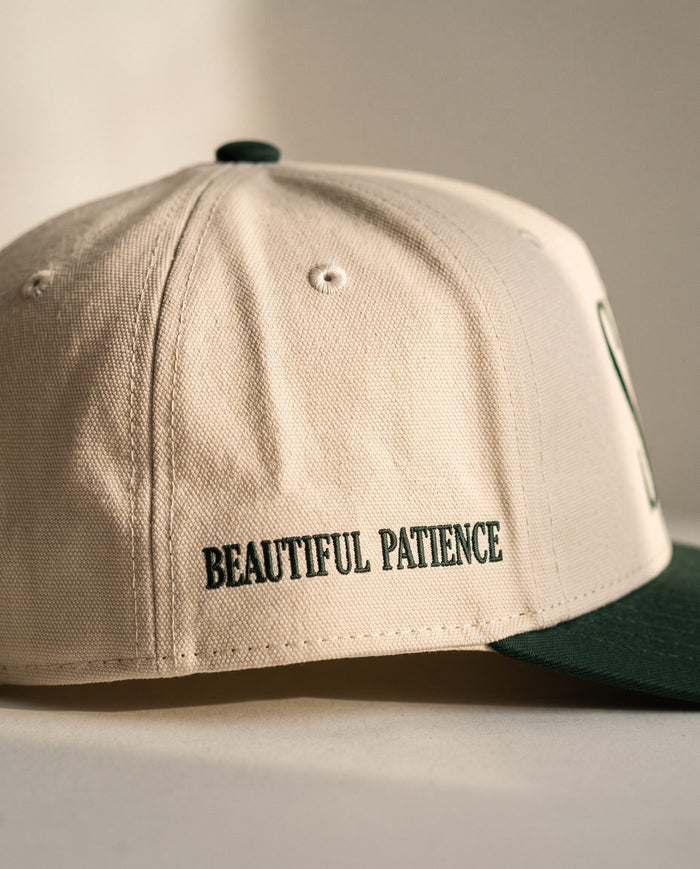 Close detail of BEAUTIFUL PATIENCE embroidered in dark green on the right side panel of the ivory Sabr Cap