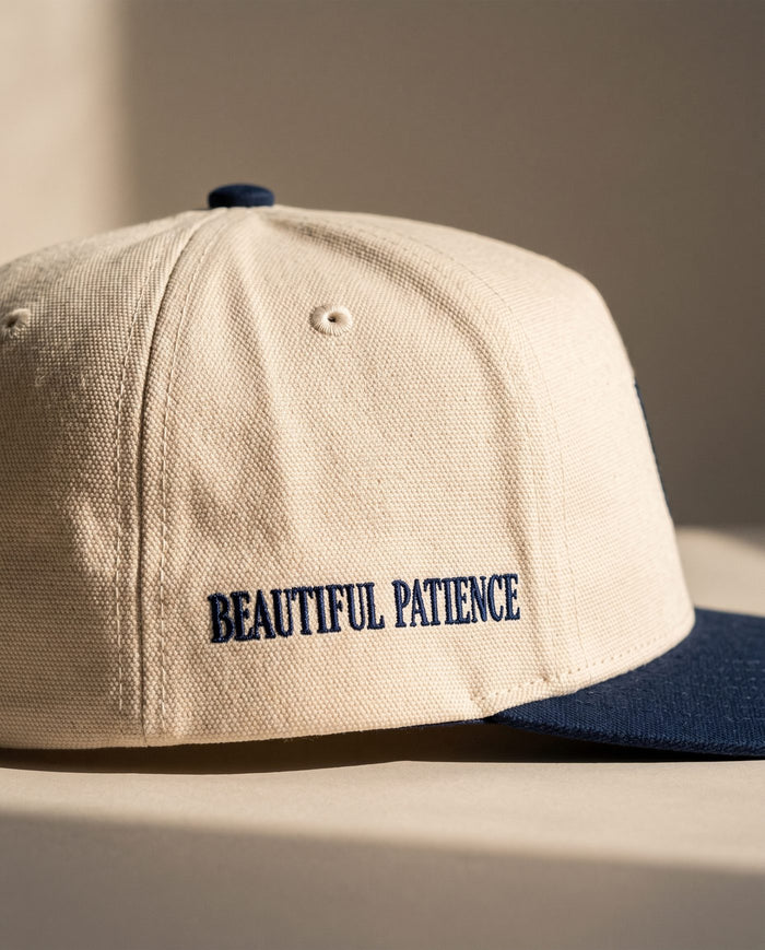 Close detail of BEAUTIFUL PATIENCE embroidered in navy on the right side panel of the ivory Sabr Cap
