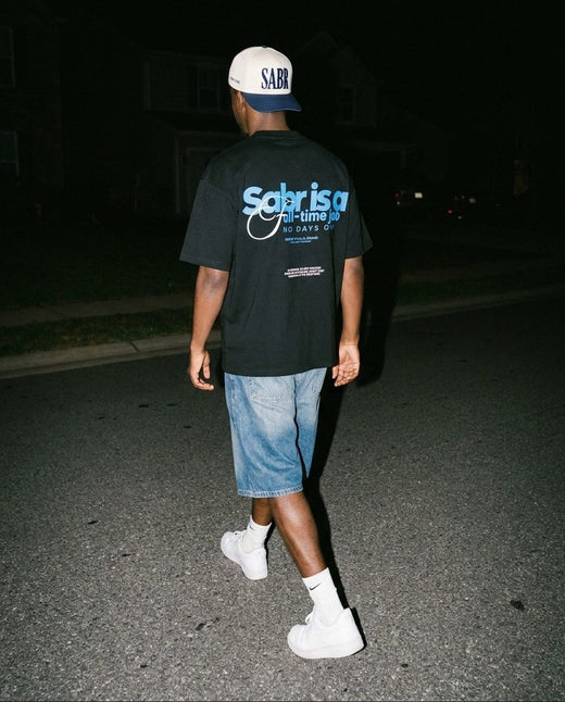 Sabr Cap in ivory with a navy brim worn with the black Full-Time Sabr tee on a night street