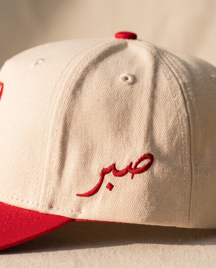Close detail of the Arabic word sabr embroidered in red on the left side panel of the ivory Sabr Cap