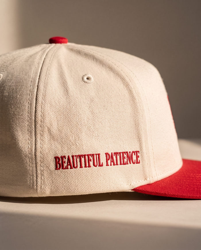 Close detail of BEAUTIFUL PATIENCE embroidered in red on the right side panel of the ivory Sabr Cap