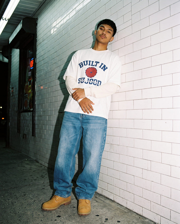 Built in Sujood white boxy tee against a white tiled bodega wall