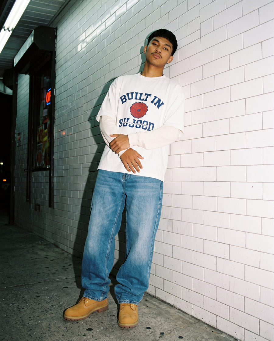 Built in Sujood white boxy tee against a white tiled bodega wall